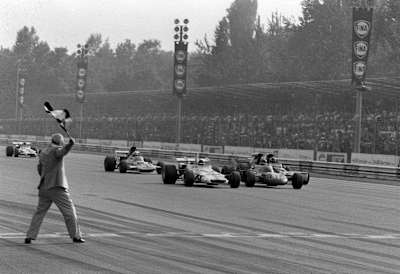 A man standing at the finish line waving the flag as two cars next to each other approach the finish