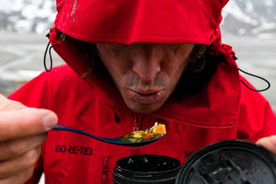 Stefan Glowacz in a red jacket blows on food to cool it down.