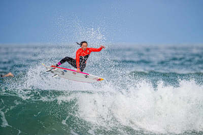 La surfeuse Carissa Moore exécute un impressionnant aerial au-dessus d'une vague lors d'une session de surf.