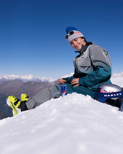At the 2025 Red Bull Performance Camp in Saas-Fee, Switzerland, Mathilde Gremaud relaxes on snowy slopes with Red Bull and Oakley gear under blue skies.