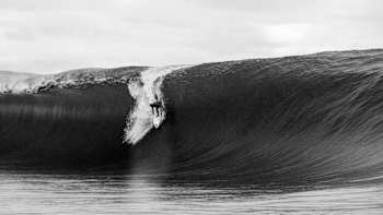 Tikanui Smith en action sur sa planche de surf sur un drop d'une vague de Teahupo'o à Tahiti.