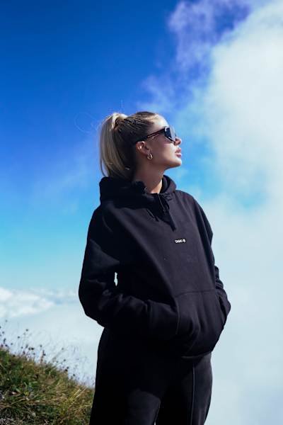Loredana steht mit einer Sonnenbrille und Hoodie in der Sonne.