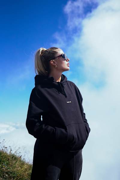 Loredana steht mit einer Sonnenbrille und Hoodie in der Sonne.