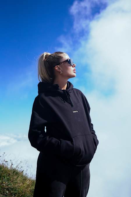 Loredana steht mit einer Sonnenbrille und Hoodie in der Sonne.