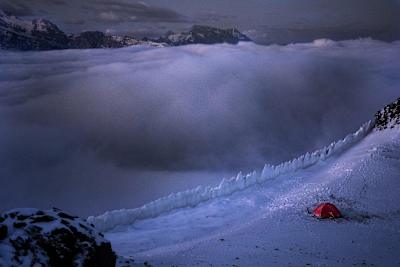 Tent on the edge of a snowy ledge high up in the mountains.