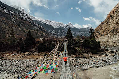 Ollie Wilkins and Rob Warner ride over a bridge towards mountains in Nepal.