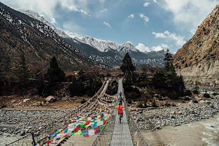 Ollie Wilkins and Rob Warner ride over a bridge towards mountains in Nepal.