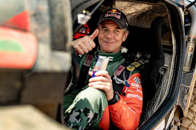 Sébastien Loeb levanta el pulgar mientras sostiene una lata de Red Bull al llegar a meta en el BP Ultimate Rally Raid Portugal 2026.
