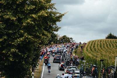 Crowds cheer as Red Bull - BORA - hansgrohe cyclists power through stage 2 of the Deutschland Tour 2025 in Essen, Germany, with support vehicles and fans crowding the road.