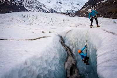 Person in glacier crevice using ice picks to climb glacier.