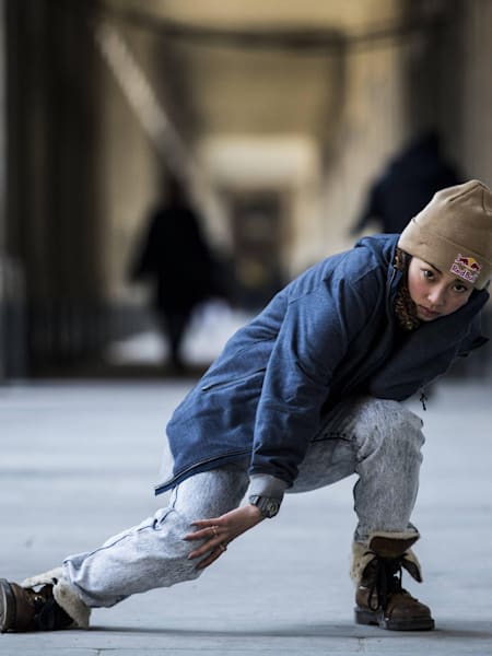 Kyoka stepping low on one leg whle grabbing the other knee for extra style. People blurry in the background.