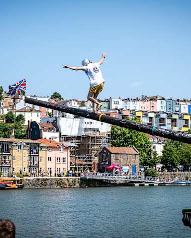 Un participant tente de courir sur un mât graissé et incliné au-dessus de l’eau lors de Red Bull Up the Mast, un défi spectaculaire qui inspire Red Bull Sur Le Mât à Saint-Malo.