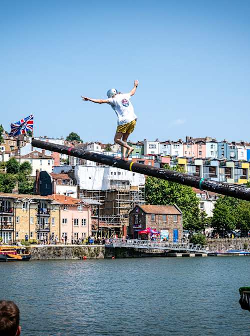 Un participant tente de courir sur un mât graissé et incliné au-dessus de l’eau lors de Red Bull Up the Mast, un défi spectaculaire qui inspire Red Bull Sur Le Mât à Saint-Malo.