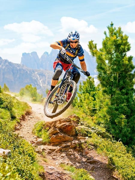Mountainbiker springt über einen Stein auf einem MTB-Trail in Südtirol.