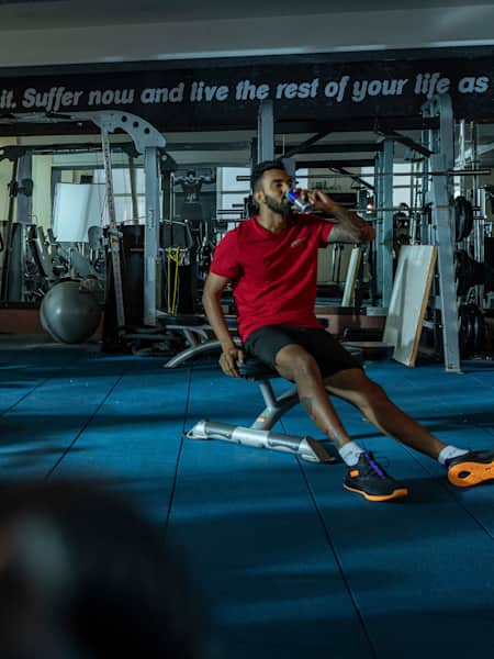 KL Rahul sips from a can of Red Bull while seated in a gym.
