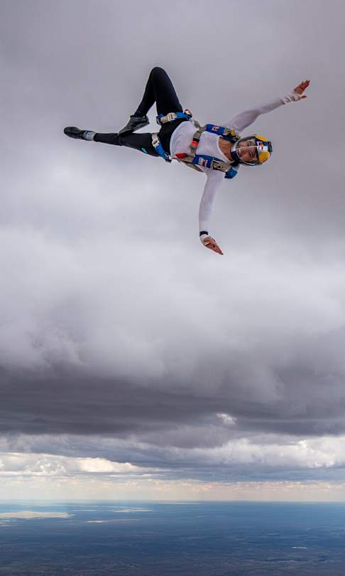 Kyra Poh is captured mid-air against dramatic clouds during the Red Bull Aerial Performance Camp in Bitterwasse, Namibia on April 26, 2026, displaying explosive skydiving energy