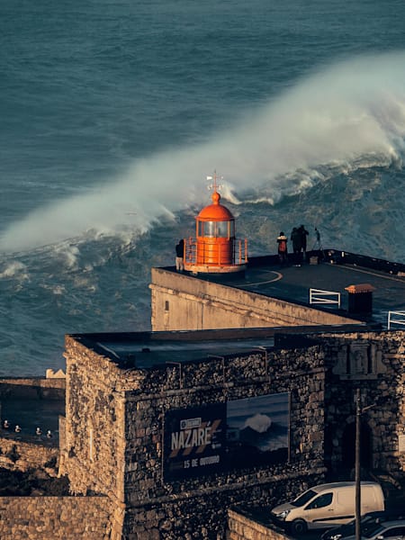 Location shot of Nazaré, Portugal with huge surf towering behind a lighthouse on January 18, 2018.