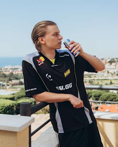 Aleksi "Aleksib" Virolainen, Haziran 2025'te Natus Vincere (NAVI) Counter-Strike 2 takımı kıyafetleri ve elinde Red Bull ile Ukrayna manzarası önünde poz veriyor