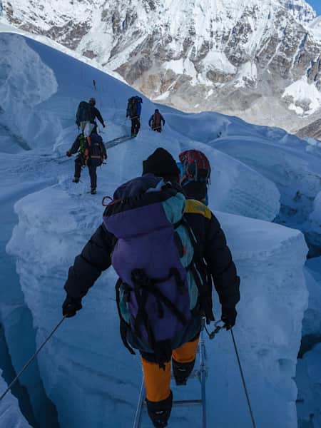 Sherpas crossing an aluminum ladder bridge above a crevasse at Mount Everest.