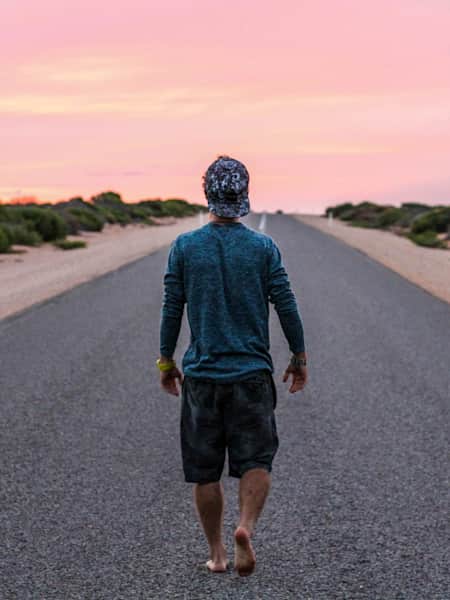 Man standing on a desert road looking at the sunset and red sky