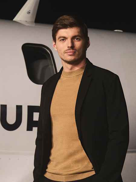Le champion du monde de F1 Max Verstappen pose avec des vêtements AlphaTauri et à côté d'un avion. 