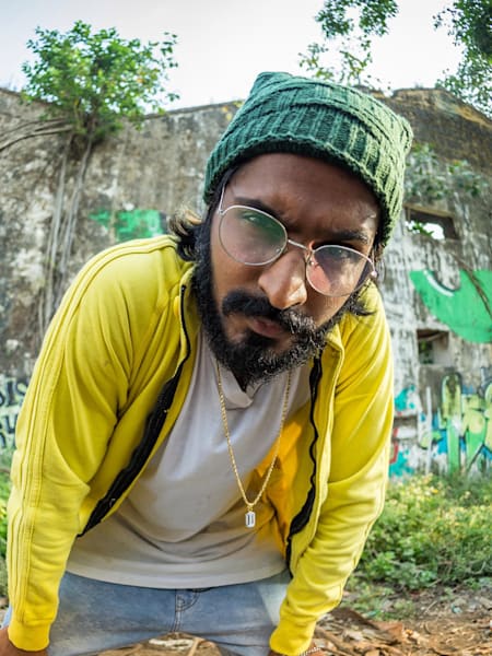 Emiway Bantai poses in front of a wall with graffiti