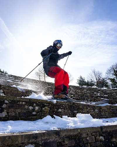 Paddy Graham powers down snow-covered stone steps during a 2023 photoshoot in the United Kingdom, spraying powder beneath his skis in spectacular winter action