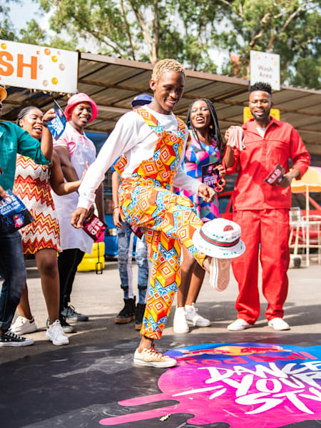 Tebza balances his hat on the tip his foot while Angyil and the crowd are watching.