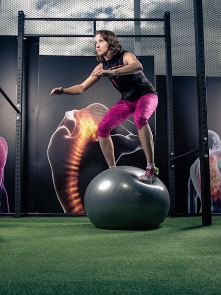 An athlete standing on a balance ball in the gym.