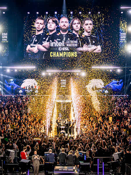 A big screen announces Team Spirit as champions of IEM Cologne 2025 with a light show and golden ticker tape falling onto a large crowd of spectators.