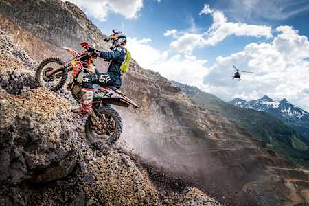 Enduro Champion Manuel Lettenbichler mit dem Bike auf einem Berg. Im Hintergrund: Ein Hubschrauber.