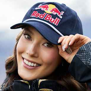 Eileen Gu showcases her signature Red Bull cap and custom jacket in Wanaka, New Zealand, during a dynamic 2025 portrait session set against breathtaking mountain scenery.