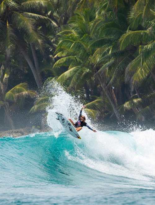 Caitlin Simmers rides a wave on her Red Bull board with palm trees in the background for filming of Now Days, a generation surf film
