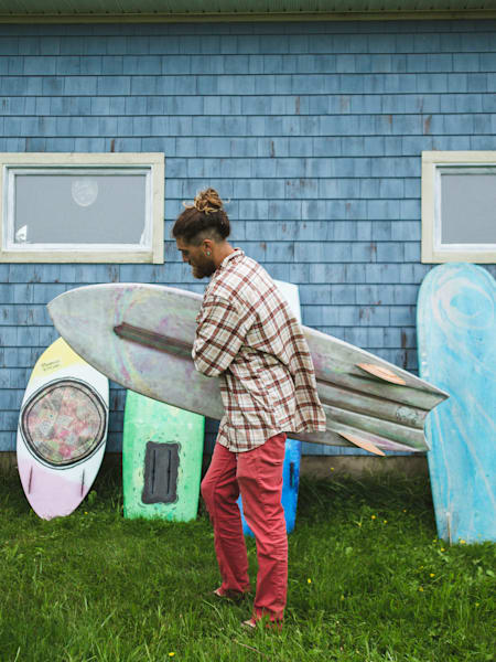 Alexis Boudreau passe devant un bâtiment avec quatre planches de surf appuyées contre l'extérieur.