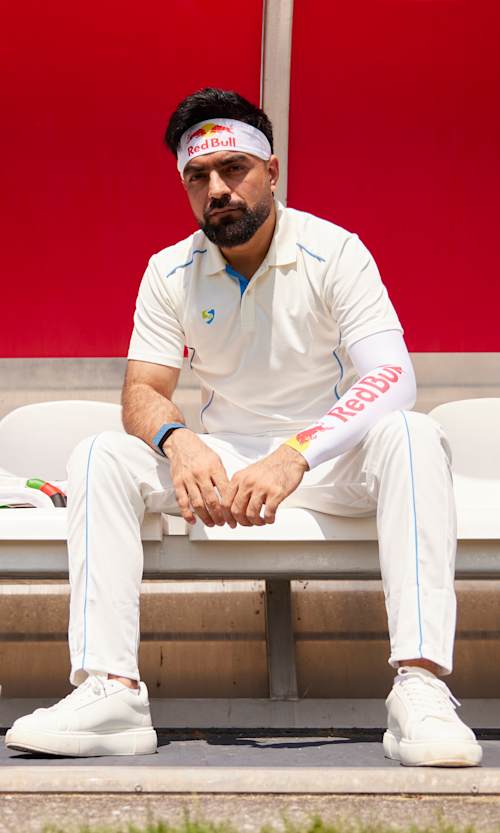 In Salzburg, Austria, July 2025, Rashid Khan Arman sits on the cricket sidelines, showcasing bold Red Bull branding on his kit and bat, embodying the brand's dynamic sporting spirit