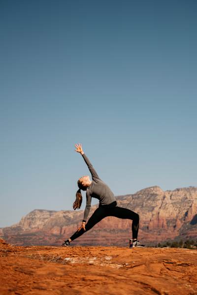 Kate Courtney in high lunge yoga pose on top of rocky terrain, clear blue skies above