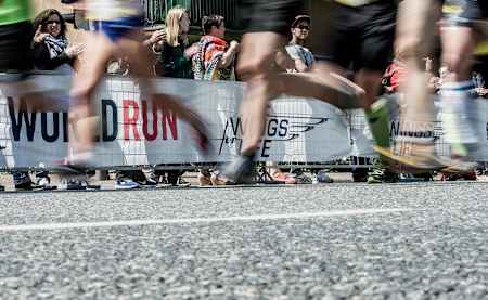 A Wings For Life World Run banner on a barricade with runners passing by