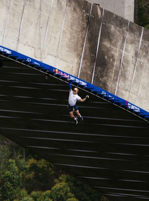 Thomas van Tonder hängt während des „Red Bull Bridge Bars“-Events im Oktober 2026 in Südafrika an einem Klettergerüst unter der Bloukrans-Brücke.