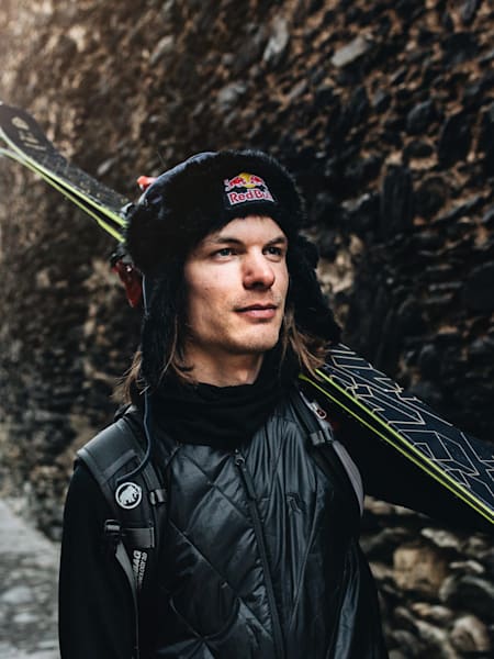 A portrait of freeride skier Kristofer Turdell in Red Bull hat carrying his skis.
