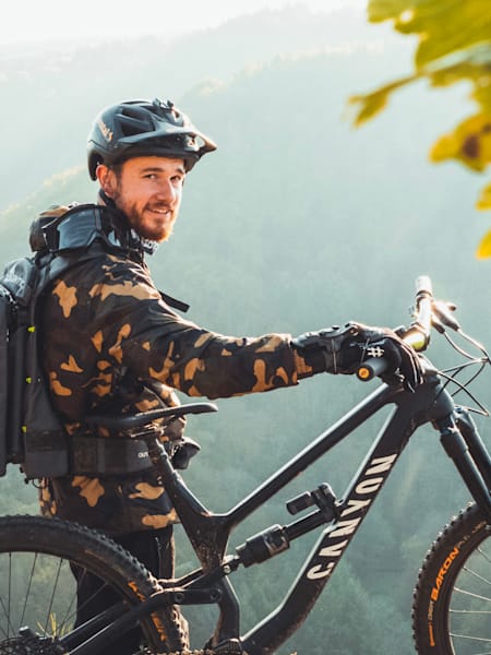 YouTuber und Mountainbike-Fahrer Fabio Schäfer posiert mit seinem Canyon Mountainbike für ein Porträt in den Bergen.