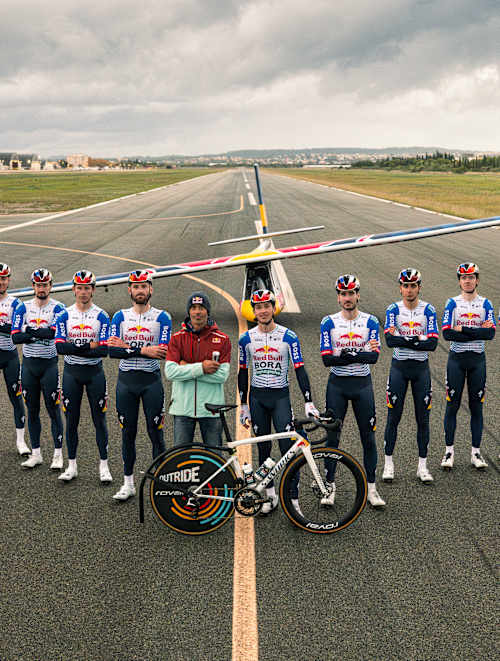 Neun Fahrer von Red Bull - BORA - hansgrohe lassen ein Flugzeug fliegen.
