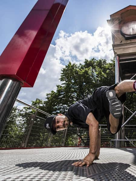 B-Boy Aya standing on his hands and showing a freeze pose with his feet. Old clock in the background