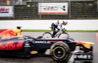 Radprofi Lotte Kopecky mit ihrem Bike auf der Rennstrecke neben einem Red Bull F1-Boliden.