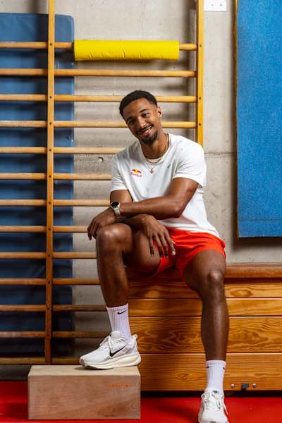 Leo Neugebauer, wearing Red Bull-branded athletics kit, sits and smiles in a gymnasium during a photo shoot in Germany in 2026.