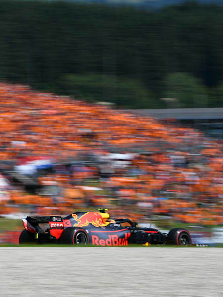 An image of Max Verstappen racing at the 2018 Formula One Grand Prix of Austria with a stand packed with orange-clad fans in the background.