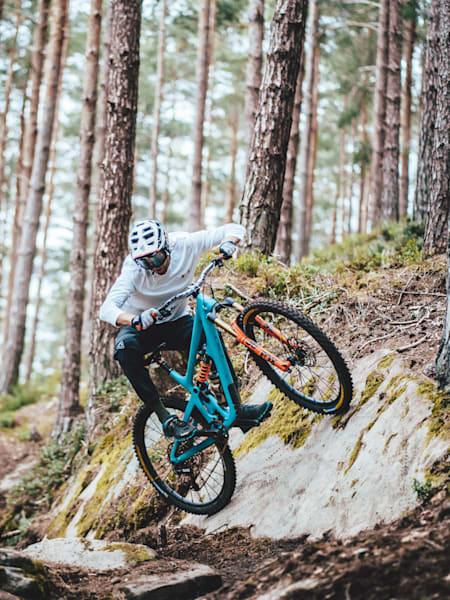 Le pilote VTT privé Thomas Lapeyrie prend un drop sur son vélo sur un sentier en forêt.