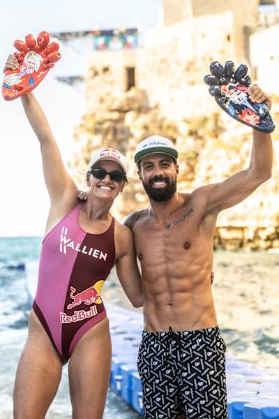 Rhiannan Iffland and Carlos Gimeno toast their win at the 2025 Red Bull Cliff Diving World Series in Polignano a Mare, Italy, raising trophies against the dramatic coastal backdrop