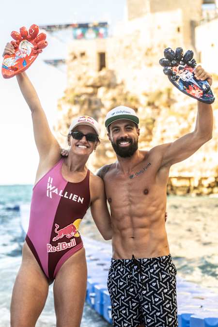 Rhiannan Iffland and Carlos Gimeno toast their win at the 2025 Red Bull Cliff Diving World Series in Polignano a Mare, Italy, raising trophies against the dramatic coastal backdrop
