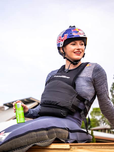 Evy Leibfarth wearing wetsuit and Red Bull helmet, sitting down and holding a green can of Red Bull Summer Edition