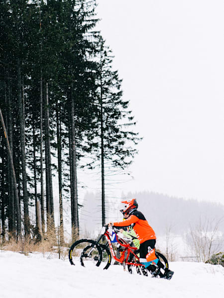 Mountain bikers pushing up the hill through snow.